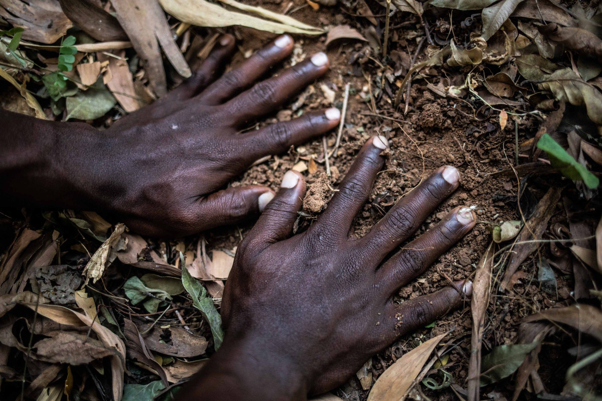 Telimele, Guinea. January 13, 2022. Lamarana, Abdoul’s brother, one of the passengers who died in Italy on January 23, 2019, <br>
touches the ground at the place where his brother was buried in his hometown. 
Abdoul’s body was repatriated to his country and rests in the cemetery of Telimele, a few meters from his home. ©︎ César Dezfuli