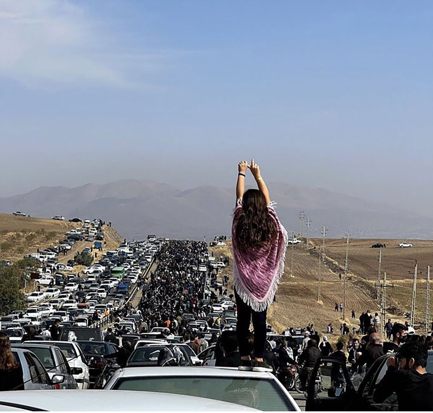 A young woman without a hijab stands on a vehicle as thousands of people make their way to the Aychi cemetery, to commemorate the 40th day of Mahsa Amini’s death, in Saqqez, her hometown in Iranian Kurdistan. Muslim tradition celebrates this date as the day of the soul’s passage to the afterlife, and the end of mourning. Saqqez, Iranian Kurdistan, October 26, 2022. Anonymous photographer.