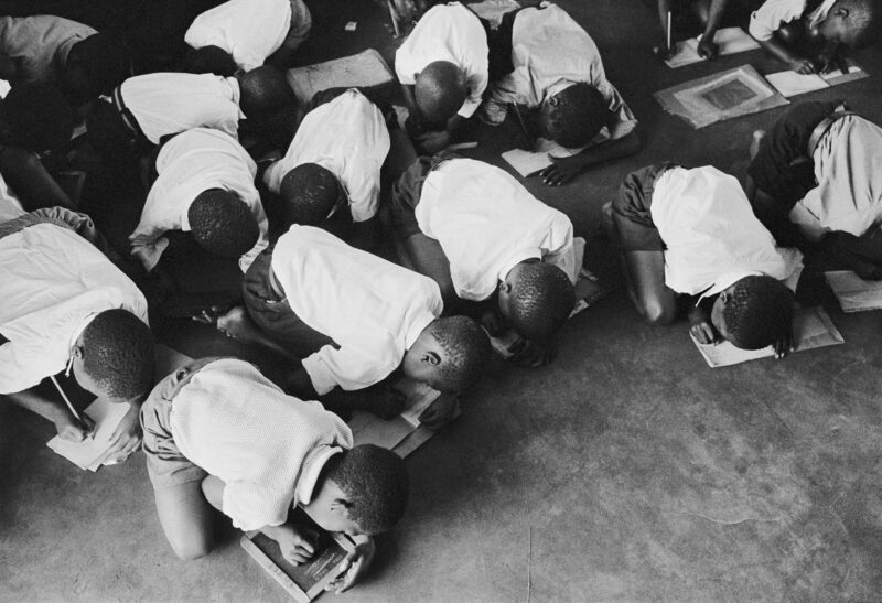 Students kneel on floor to write. Government is casual about furnishing schools for blacks. South Africa, 1960s. © Ernest Cole/ Magnum Photos